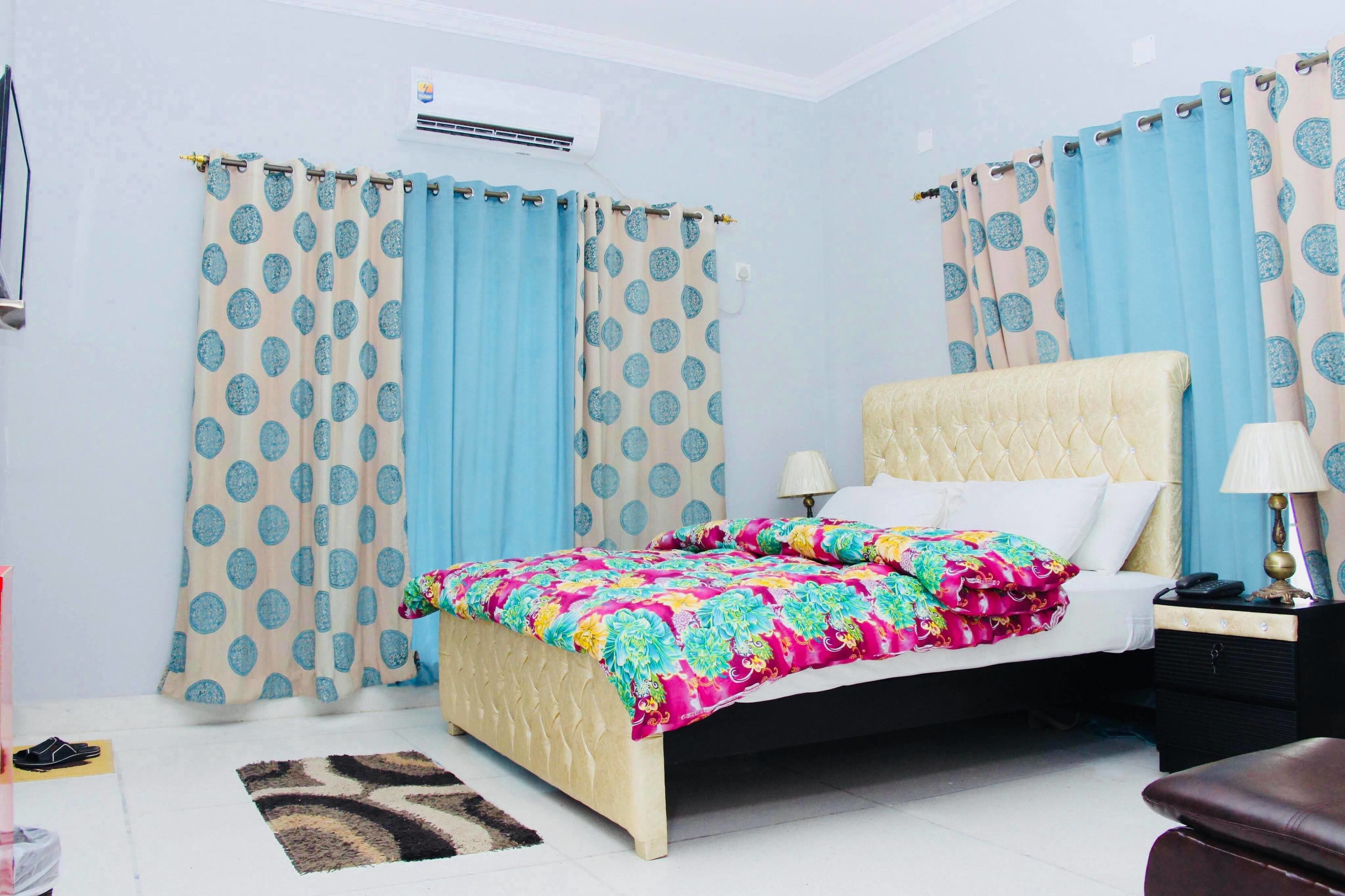 A bedroom with a bed, curtains, a bedside table, and a lamp.