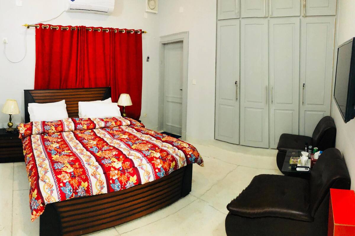 A bedroom with a bed, a nightstand, a TV, a wardrobe, and a desk with a chair.