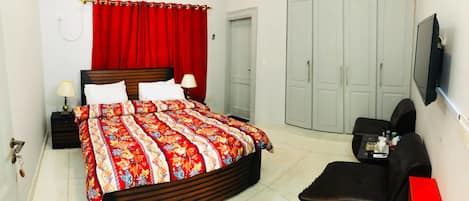 A bedroom with a bed, a nightstand, a TV, a wardrobe, and a desk with a chair.