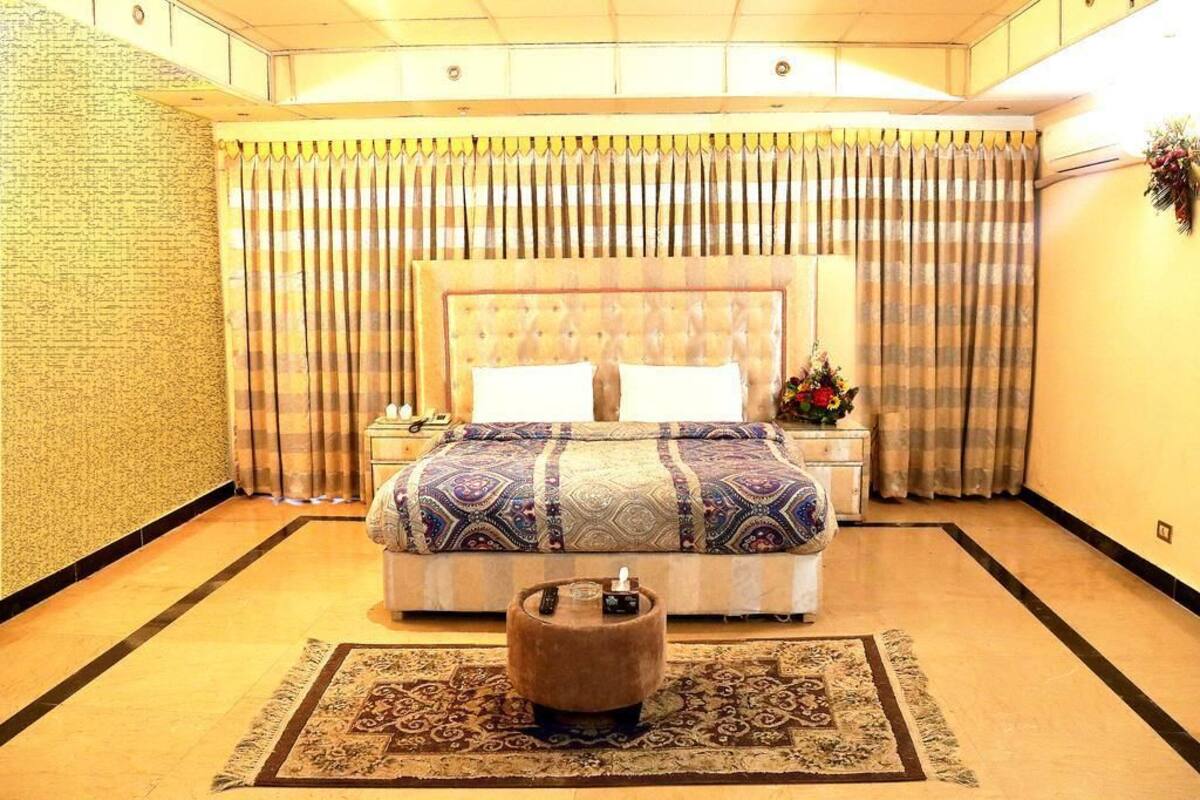 A hotel room with a large bed, a nightstand, a small table, and a decorative rug.