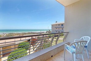 A balcony with a view of the beach, white chairs, and a railing. - Neptune Isle 214 (Cape Town)