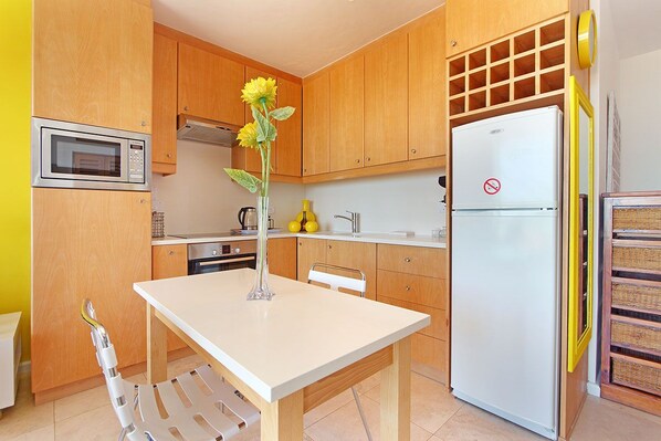 A kitchen with wooden cabinets, a microwave, a refrigerator, a sink, and a table with a vase of flowers. - Neptune Isle 214 (Cape Town)