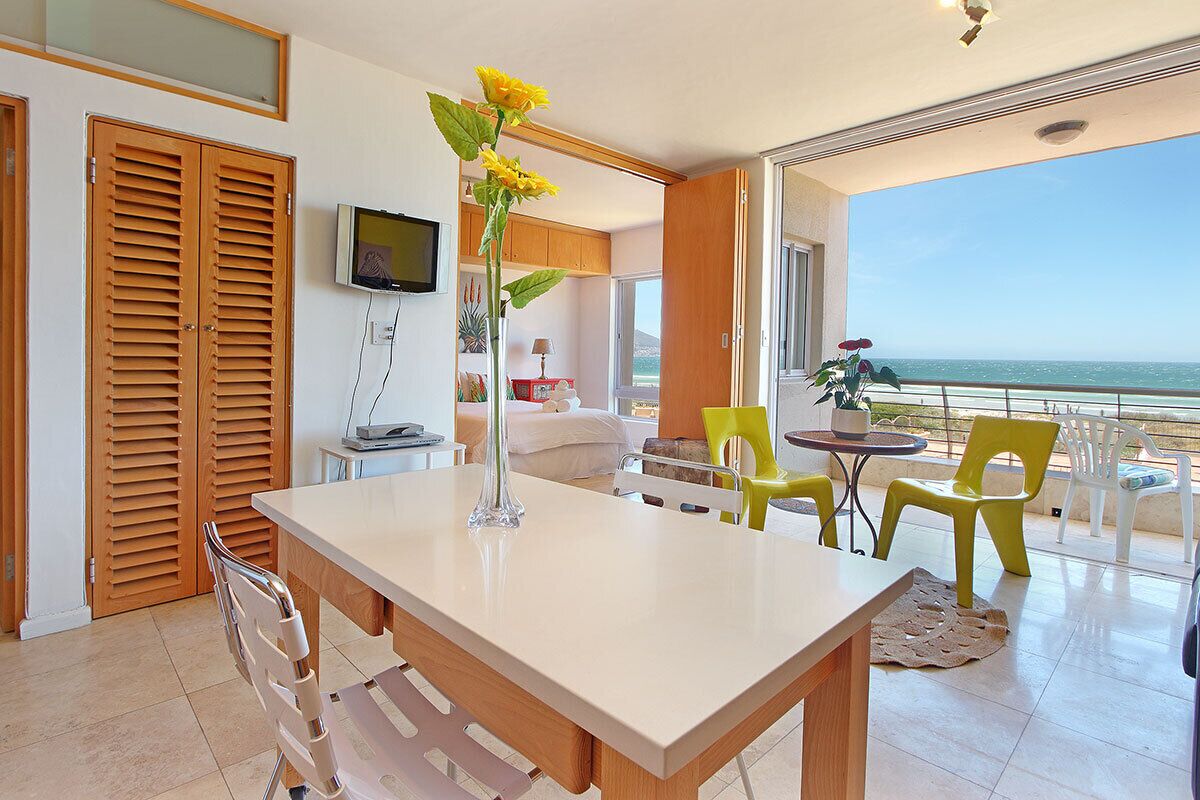 A modern room with a dining table, chairs, a TV, and a view of the ocean.
