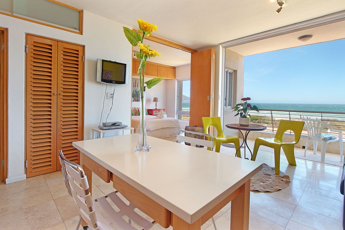 A modern room with a dining table, chairs, a TV, and a view of the ocean.