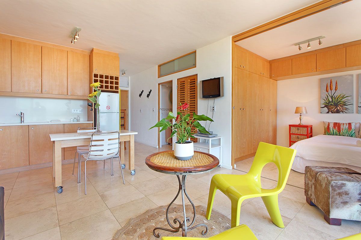 A compact kitchen with a dining area, a small table with a potted plant, and a bed with a nightstand.