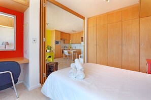 A bedroom with a bed, a desk, and a kitchenette. - Neptune Isle 214 (Cape Town)