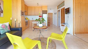 A modern kitchen with wooden cabinets, a microwave, and a refrigerator. There is a dining table with chairs and a potted plant. - Neptune Isle 214 (Cape Town)