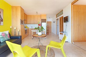 A modern kitchen with wooden cabinets, a microwave, and a refrigerator. There is a dining table with chairs and a potted plant. - Neptune Isle 214 (Cape Town)