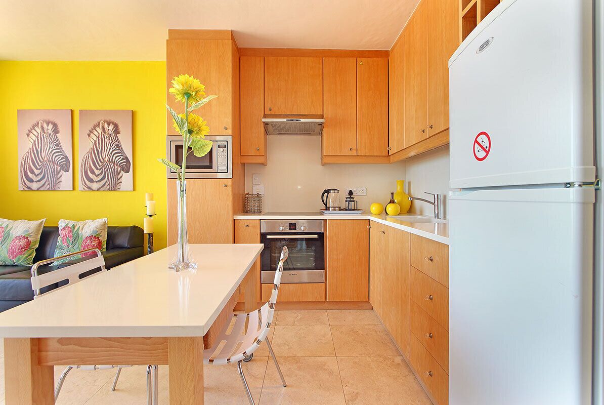 A modern kitchen with wooden cabinets, a white refrigerator, and a dining area with a table and chairs.