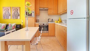 A modern kitchen with wooden cabinets, a white refrigerator, and a dining area with a table and chairs. - Neptune Isle 214 (Cape Town)