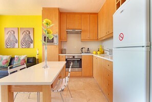 Una cocina moderna con armarios de madera, un refrigerador blanco y una zona de comedor con una mesa y sillas.