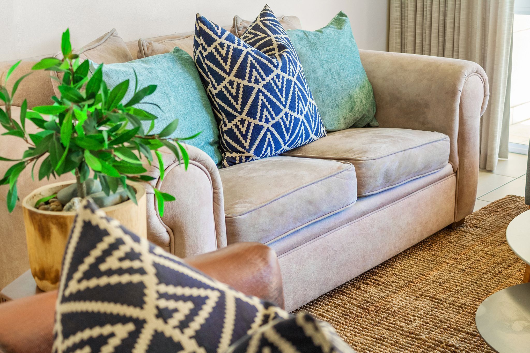 Un canapé beige agrémenté de coussins à motifs, une plante en pot et un tapis tissé dans un salon.