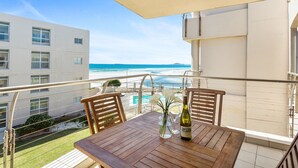 A balcony with a wooden table, chairs, a vase with flowers, and a bottle of wine. - Lagoon Beach 231 (Cape Town)