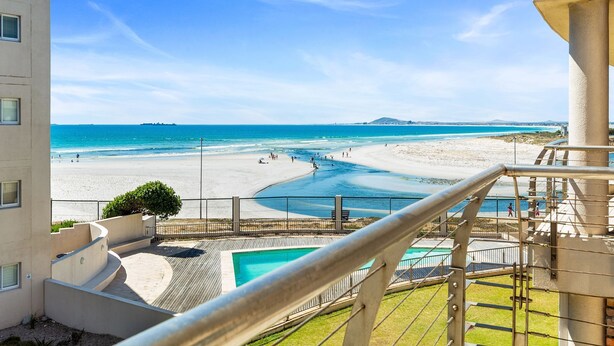 A view of a beach from a balcony with a pool and a staircase. - Lagoon Beach 231 (Cape Town)