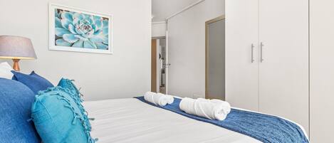Uma cama bem arrumada com roupa de cama azul e branca, um cobertor azul e um travesseiro azul.