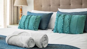 A neatly made bed with rolled white towels, a blue blanket, and teal pillows with frayed edges. - Lagoon Beach 231 (Cape Town)
