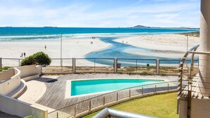 A beach view from a balcony with a pool and a fence. - Lagoon Beach 231 (Cape Town)