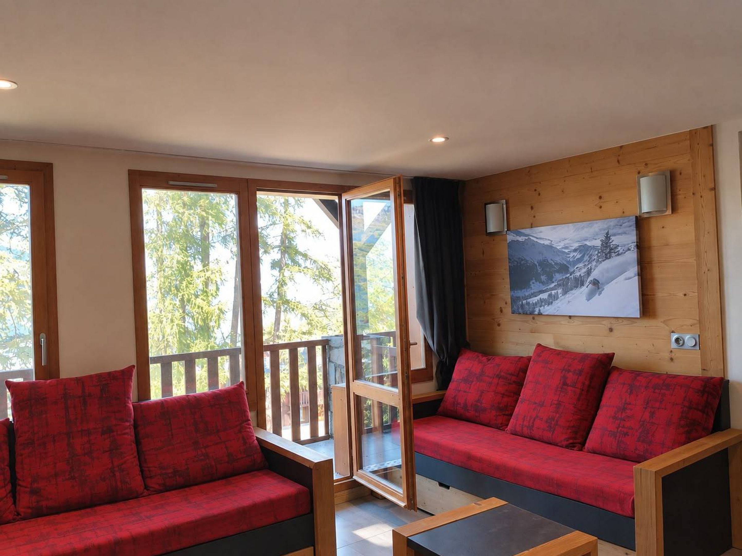 A room with a wooden wall, a painting, and a red sofa with matching cushions.