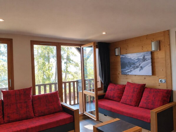 A room with a wooden wall, a painting, and a red sofa with matching cushions.