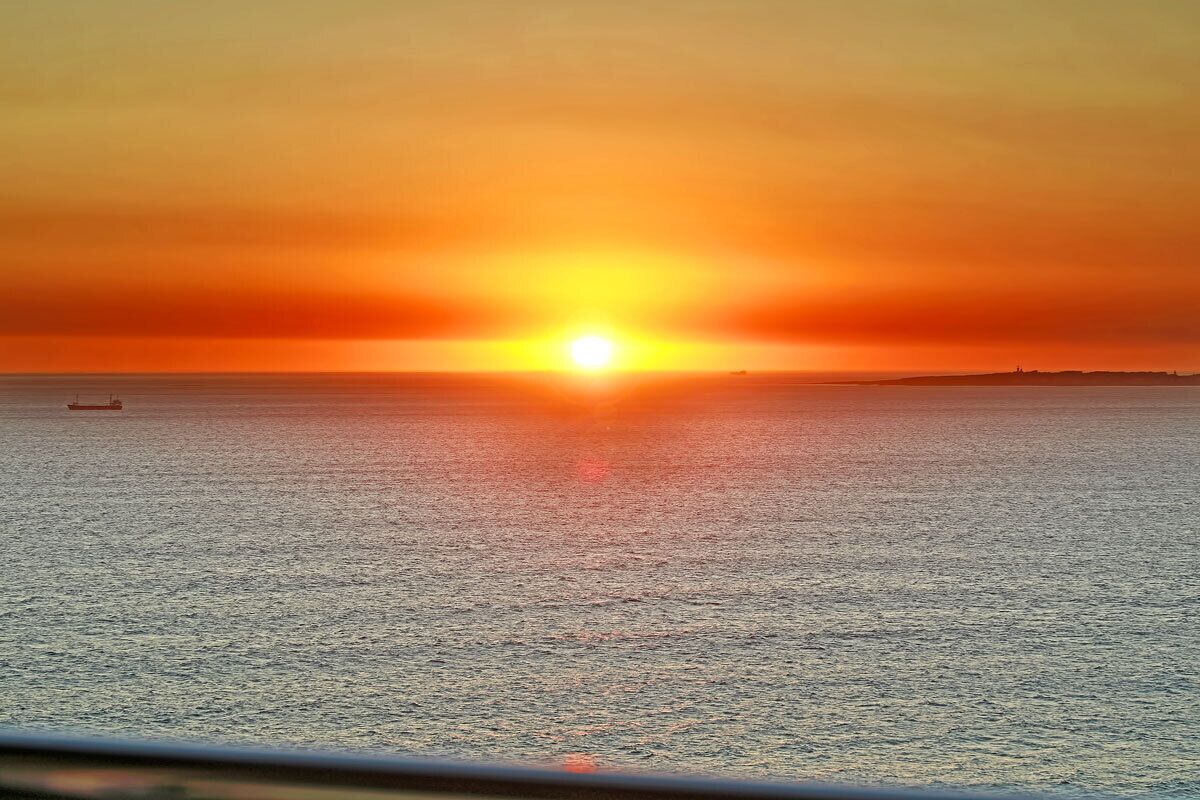 A sunset over a calm sea with a distant shoreline.