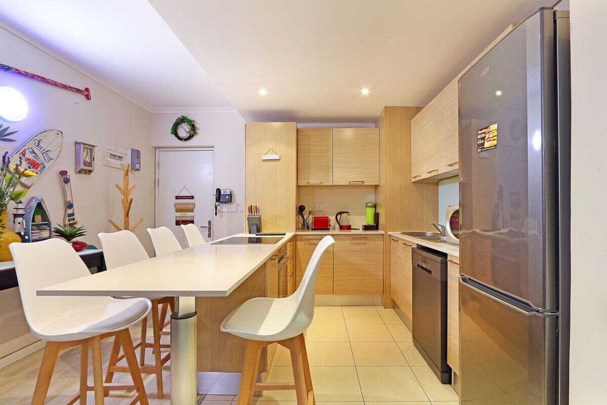A modern kitchen with a dining table, chairs, wooden cabinets, a refrigerator, and a dishwasher.