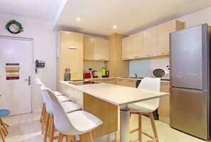 A modern kitchen with a central island, wooden cabinets, a stainless steel refrigerator, and bar stools. - Horizon Bay 1201 (Cape Town)