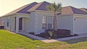 A single-story house with a front garage, a small front yard with a palm tree, and a sloped roof. - Ly239890 - Emerald Island Resort - 4 Bed 3 Baths Villa (Kissimmee)