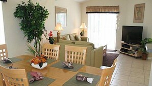 A dining area with a wooden table and chairs, a large potted plant, and a television in the background. - Ly239890 - Emerald Island Resort - 4 Bed 3 Baths Villa (Kissimmee)