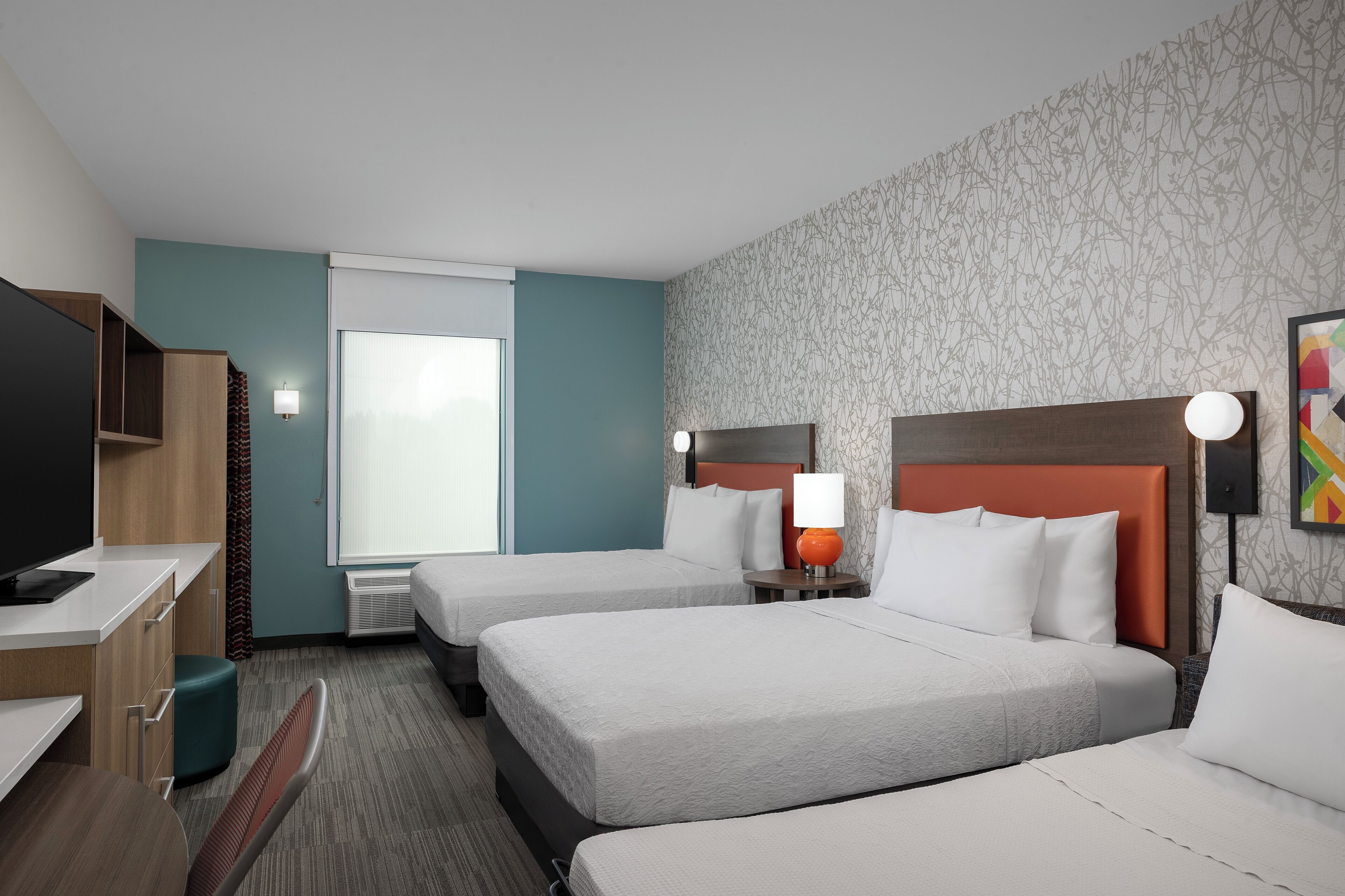 A hotel room with two beds, a desk, a TV, and a window.