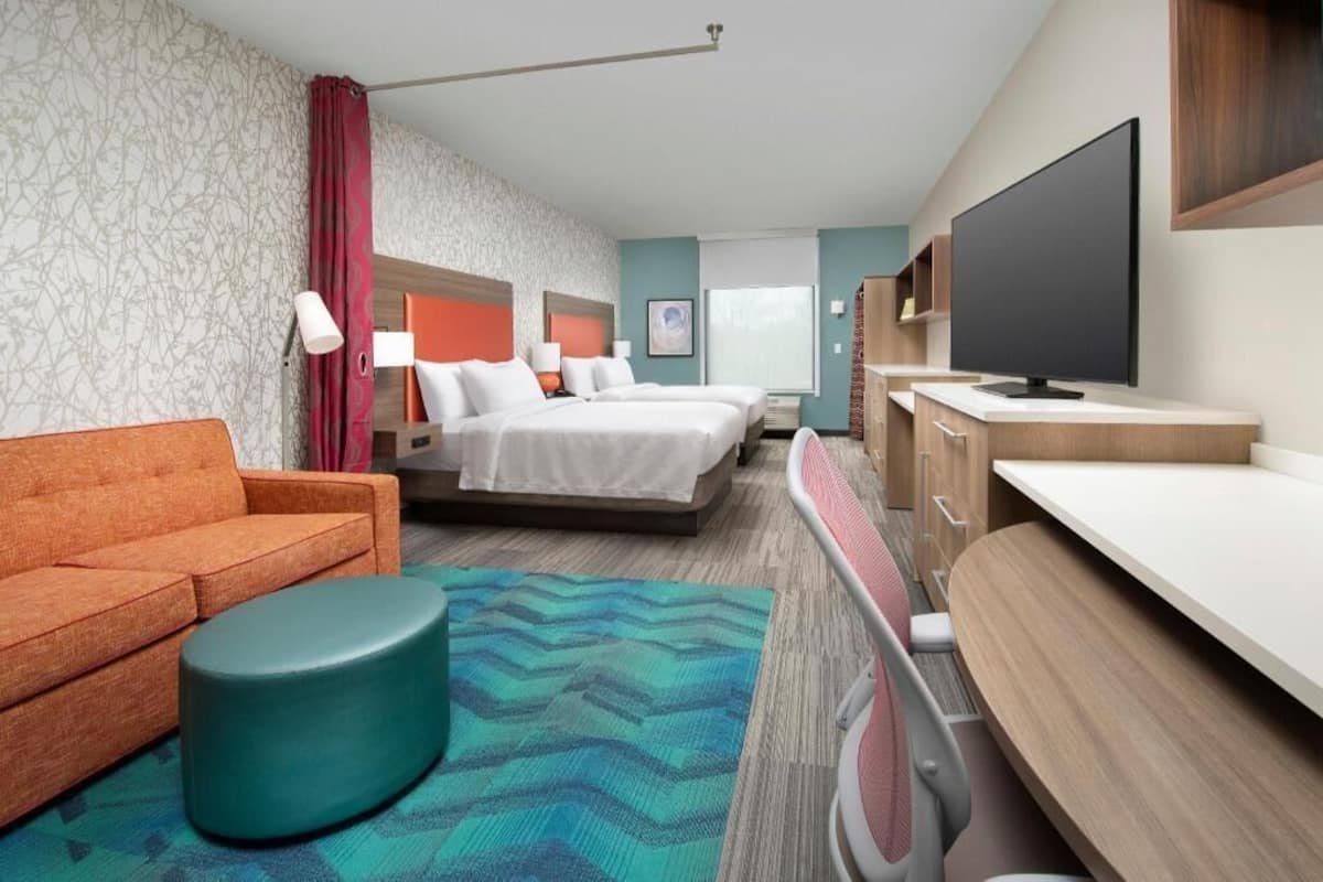 A hotel room with two beds, a sofa, a TV, a desk, and a bathroom.