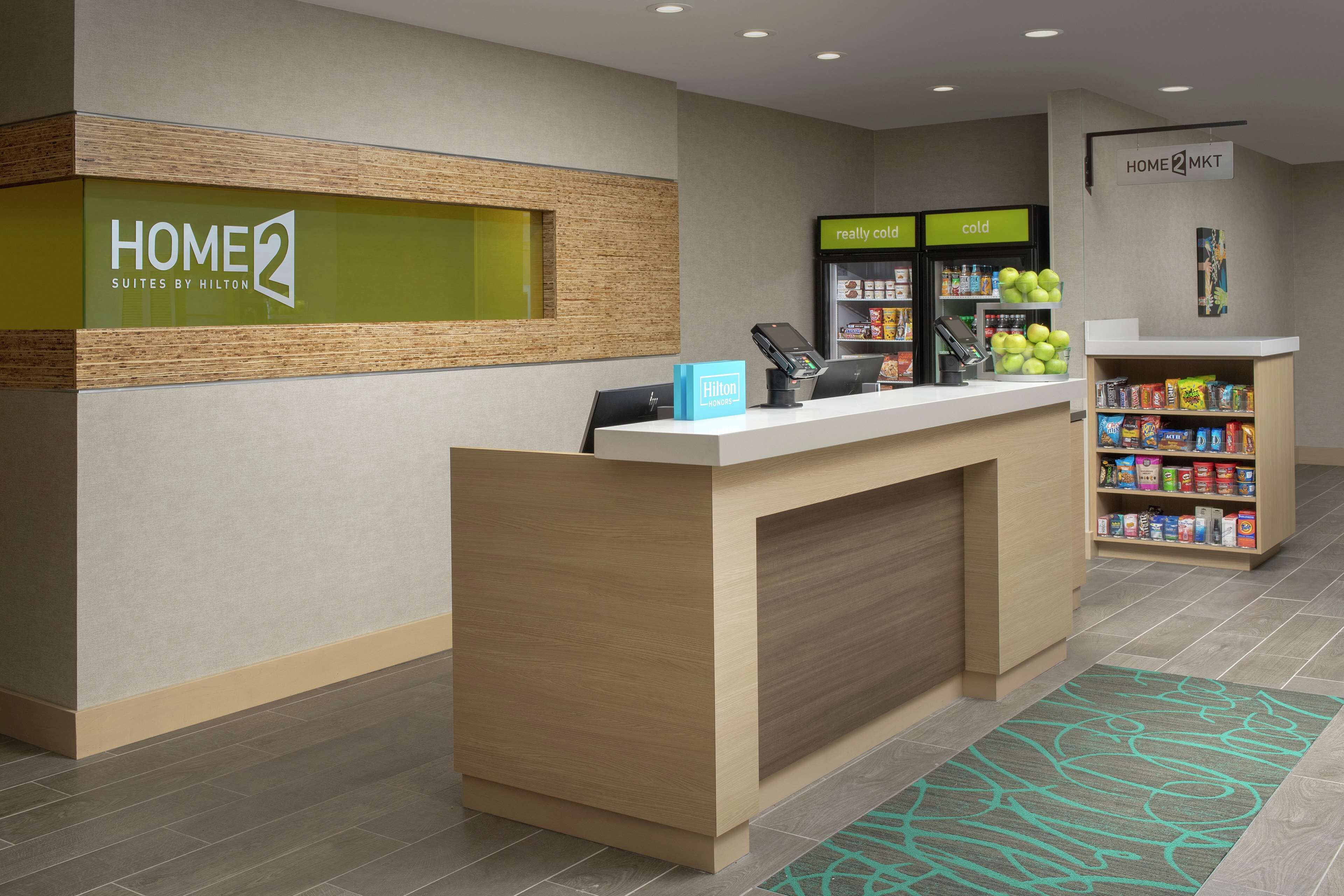 A hotel reception area with a reception desk, a minibar, and a self-service beverage station.