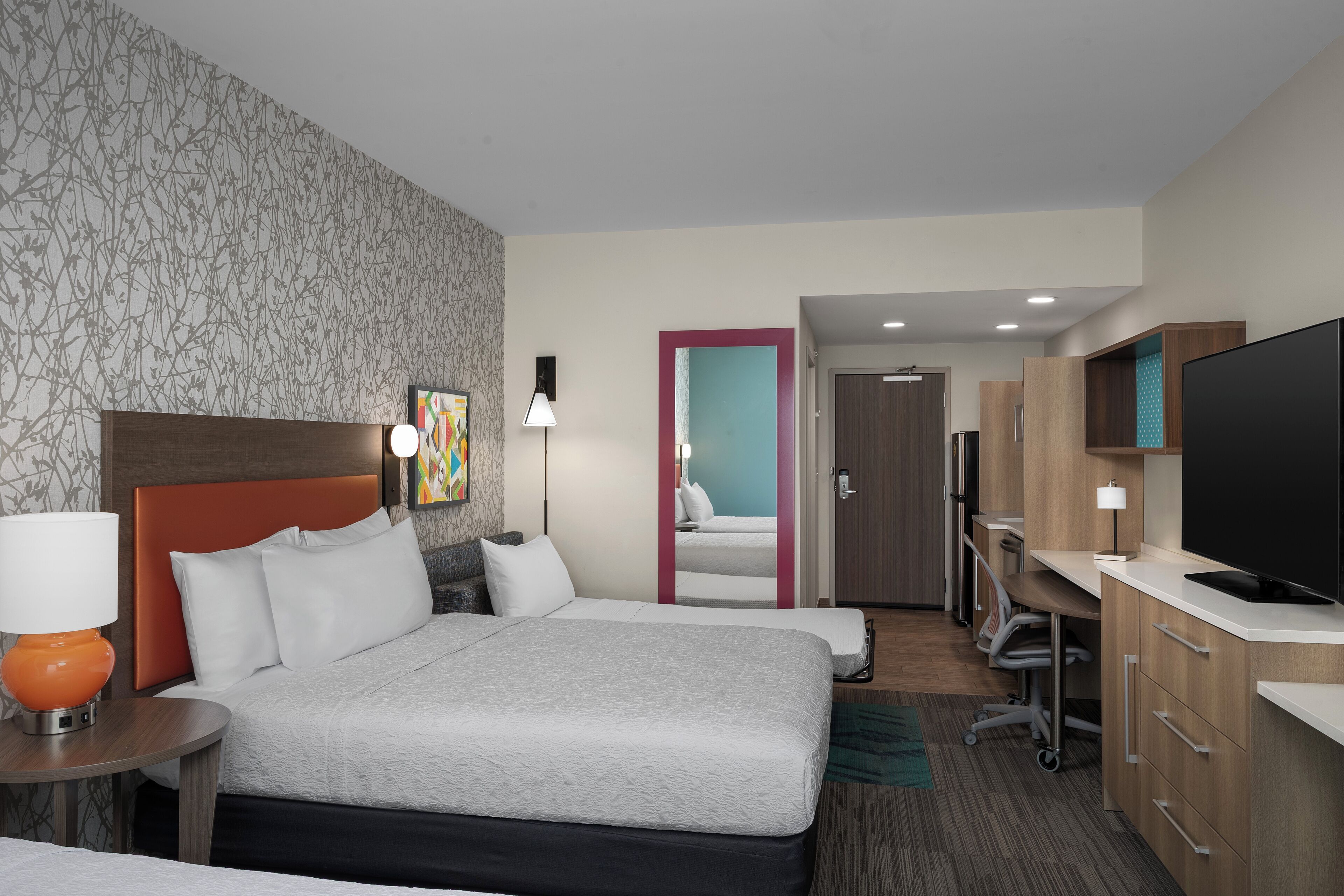 A hotel room with a large bed, a desk with a computer, a television, and a bathroom visible through an open door.