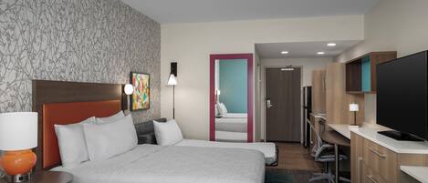A hotel room with a large bed, a desk with a computer, a television, and a bathroom visible through an open door.