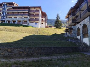 A multi-story hotel with balconies, stone walls, and a grassy hillside. - Renovated studio near slopes with wellness, pets allowed (La Plagne Montchavin Les Coches)