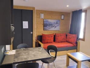 A small, cozy room with a bed, a table, and a chair. There is a painting on the wall and a window with curtains. - Renovated studio near slopes with wellness, pets allowed (La Plagne Montchavin Les Coches)