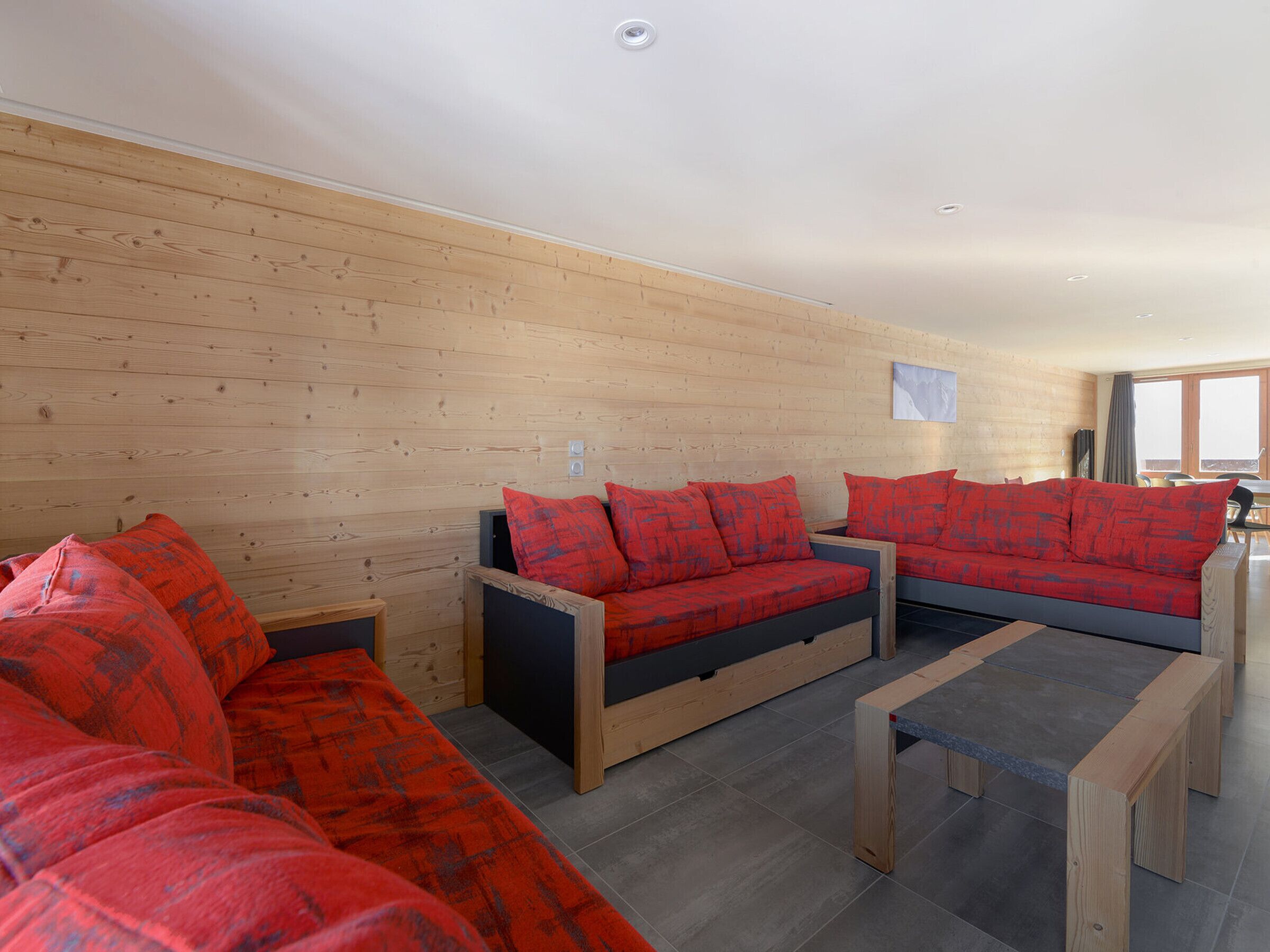 Een moderne woonkamer met houten lambrisering, twee banken met rode kussens, en een kleine houten tafel.