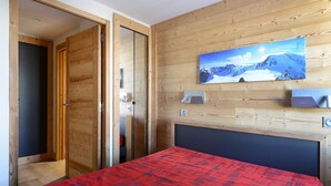 Ein Schlafzimmer mit Holzwand, einem Bett mit roter Decke, einem Gemälde von einer Berglandschaft und einer Holztür.