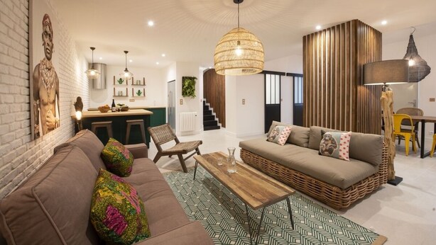 A modern living room with a brown sofa, a wicker coffee table, and a hanging woven light fixture. - Out of Africa, 4BR/3BA, 8 people (París)
