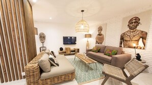 A modern living room with a sofa, a coffee table, and a wicker chair. There is a television mounted on the wall and a statue on the right side. - Out of Africa, 4BR/3BA, 8 people (París)