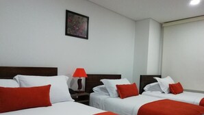Habitació d'hotel amb dos llits, amb roba de llit blanca i detalls vermells, una tauleta de nit amb una làmpada vermella i un quadre al mur.