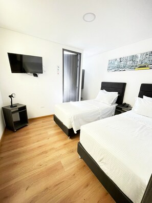 Quarto de hotel com duas camas, televisão, secretária e porta.
