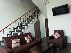 A living room with a staircase, a flat-screen TV mounted on the wall, and two sofas with patterned cushions. - Hotel Portal de los Andes (Bogotá)