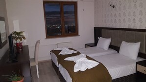 A hotel room with a bed, a desk, a chair, a potted plant, and a window with a city view. - Cankaya Konagi (Ankara)