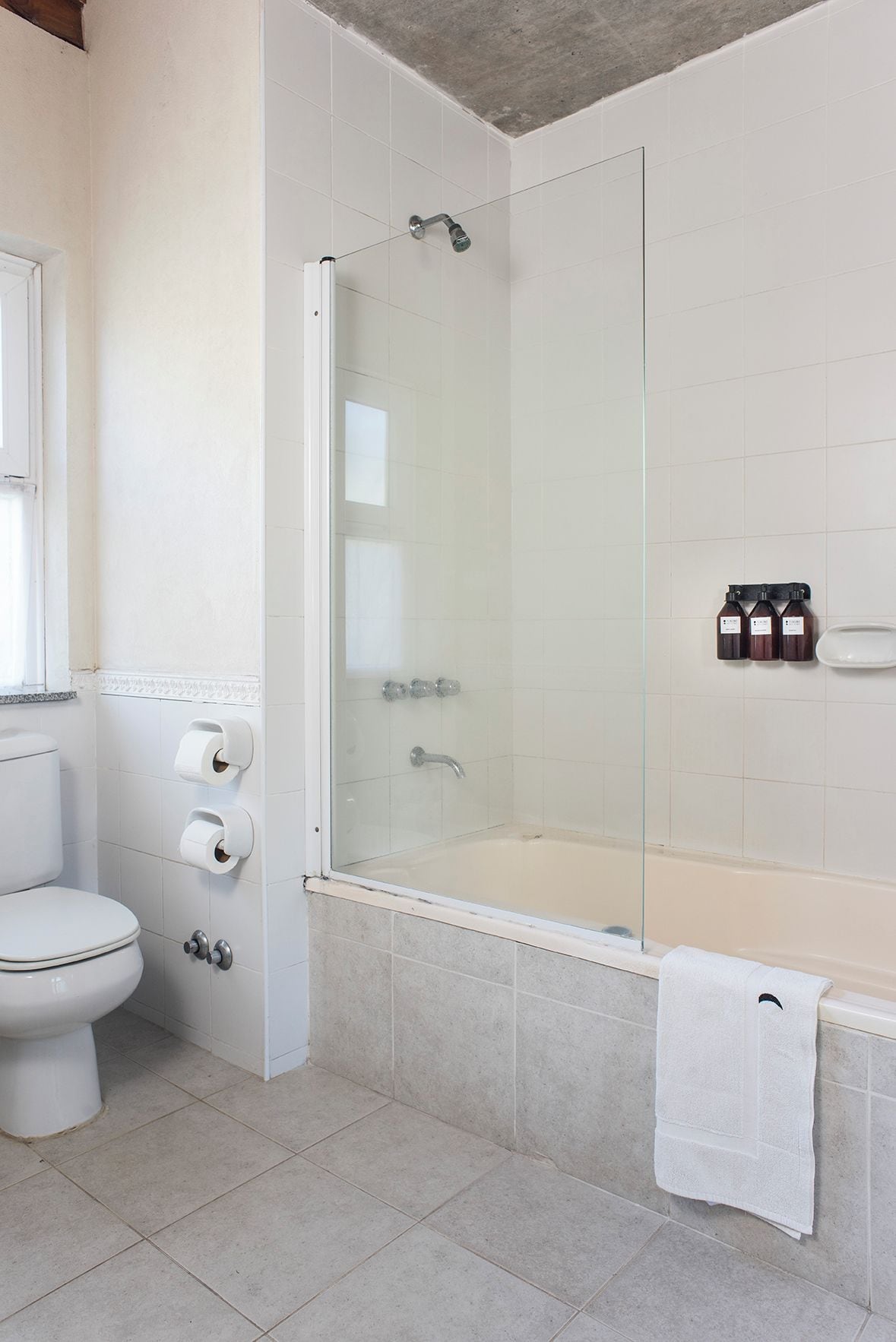 A modern bathroom with a glass-enclosed shower, a white toilet, and a bathtub with a towel.