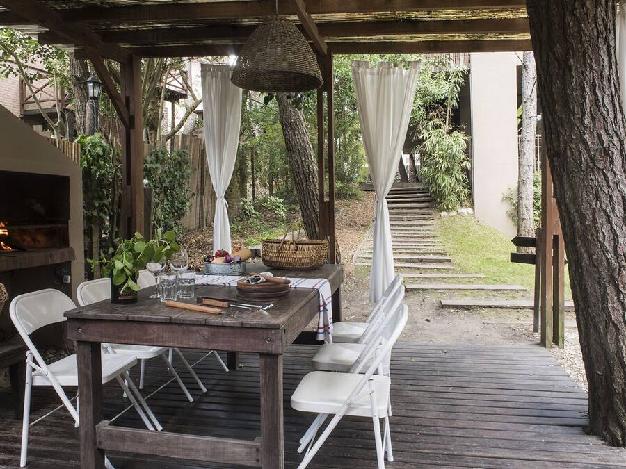 An outdoor patio with a wooden table and chairs, a hanging light fixture, and a fire feature.