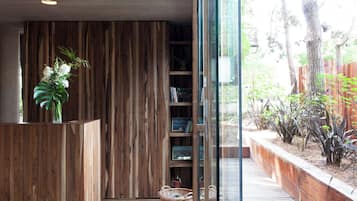 A wooden reception desk with a vase of flowers, a bookshelf with books, and a view of a garden through a glass door.