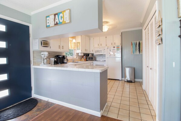 A modern kitchen with a central island, white cabinets, and a 'BEACH' sign.