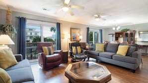 A spacious living room with a gray sofa, a red armchair, a glass coffee table, and a ceiling fan.