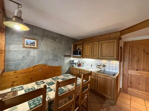 Een gezellige keuken met een stenen muur, houten kasten, een eettafel met stoelen en een hangende lamp.