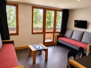 A room with a sofa, a small table, a TV, and large windows. - Bright renovated apartment - Near slopes, pets allowed (La Plagne Montchavin Les Coches)